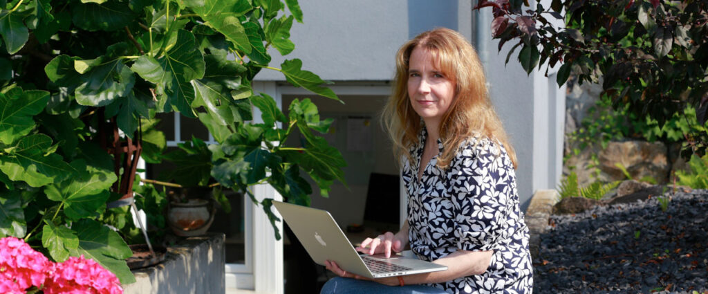 über-mich-Seite. Foto von Silke Wengenroth-Lippke draußen mit Laptop auf dem Schoß